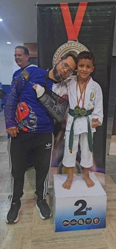 Karateka infantil junto a su entrenador en un podio luego de que el niño recibir medalla