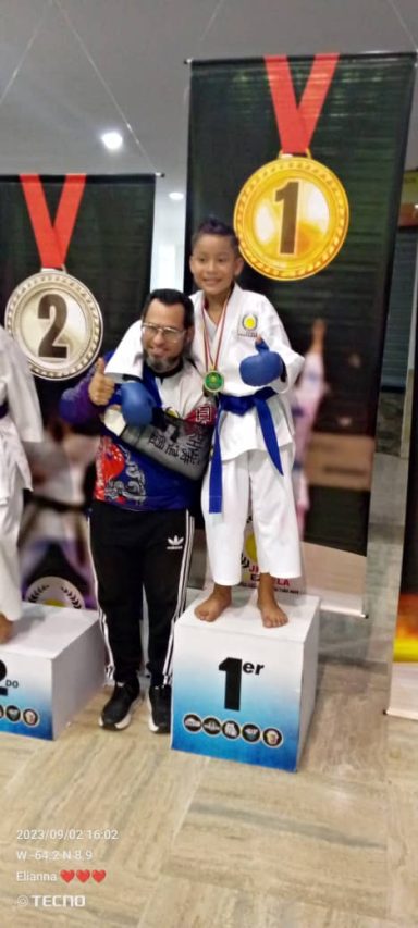 Alumno feliz recibe medalla junto a su entrenador de karate